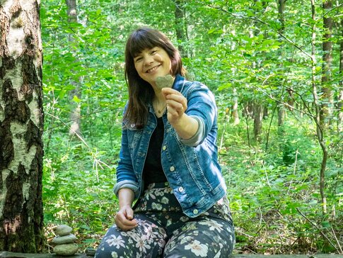 Hier sehen Sie eine braunhaarige Frau, die ein Herz in der Natur in der Hand hält. 