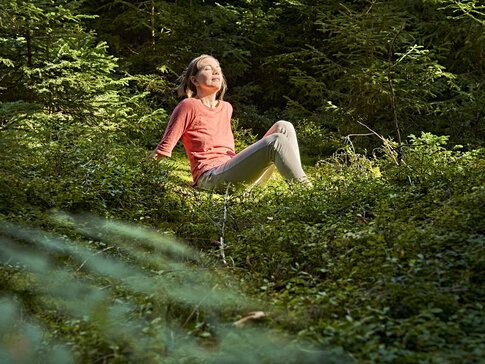 Hier sehen Sie Gesundes Bayern Waldexpertin Nathalie Elitzer beim Waldbaden mit Sonnenschein im Gesicht.